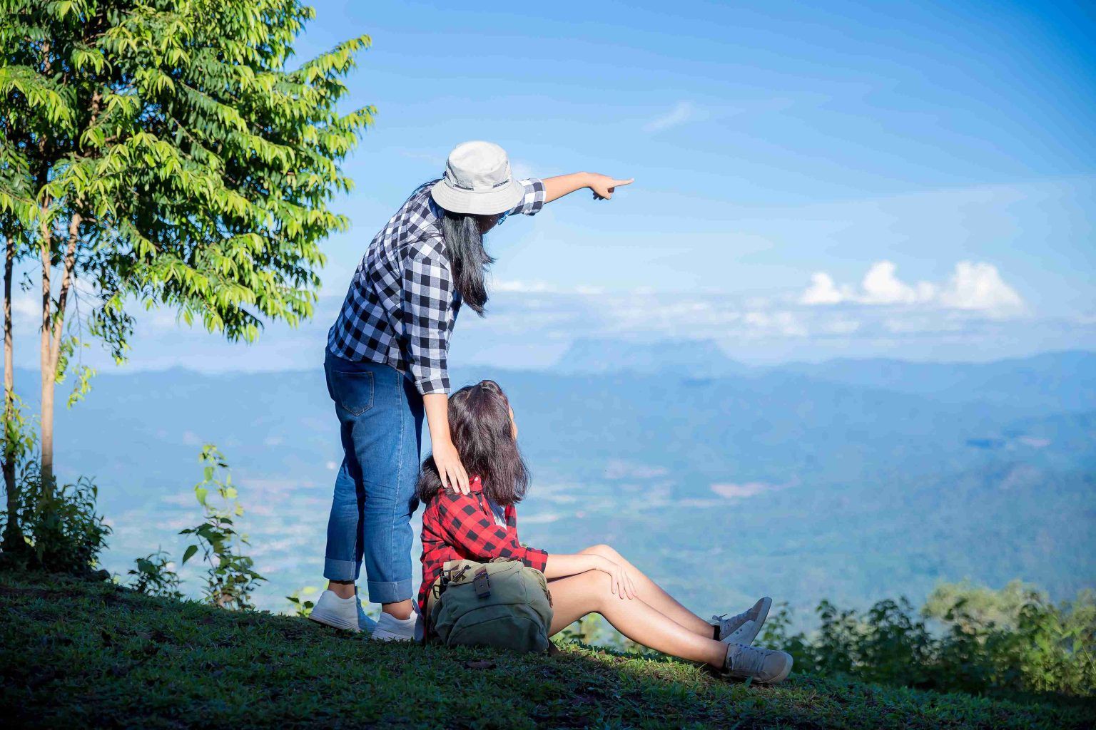 Two women on a mountain viewpoint, one pointing at the scenic landscape.